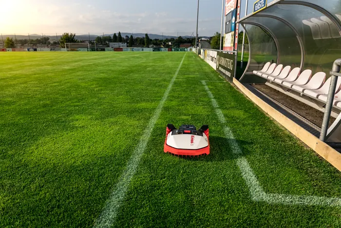 Kress Mähroboter mäht einen Fußballplatz entlang der Seitenlinie vor der Trainerbank